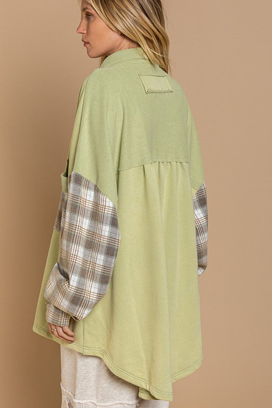 A person wearing the Long Sleeve With Plaid Detail Sleeve Shacket in brown, featuring plaid details on the sleeves and a matching pocket, paired with a white top underneath and a wide-brimmed hat—perfect for transitional weather.