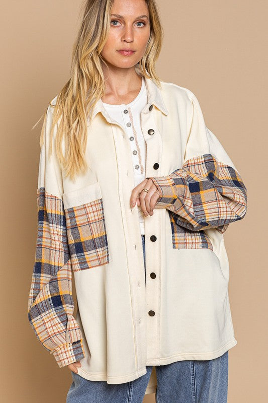 A person wearing the Long Sleeve With Plaid Detail Sleeve Shacket in brown, featuring plaid details on the sleeves and a matching pocket, paired with a white top underneath and a wide-brimmed hat—perfect for transitional weather.