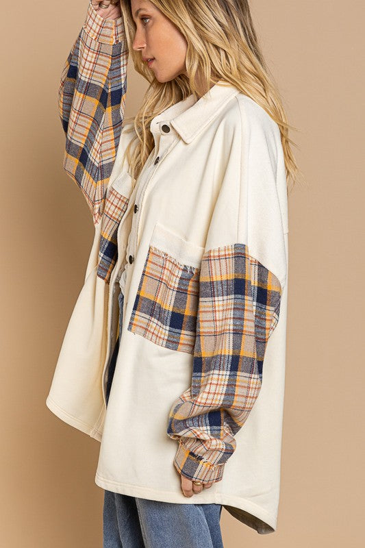 A person wearing the Long Sleeve With Plaid Detail Sleeve Shacket in brown, featuring plaid details on the sleeves and a matching pocket, paired with a white top underneath and a wide-brimmed hat—perfect for transitional weather.