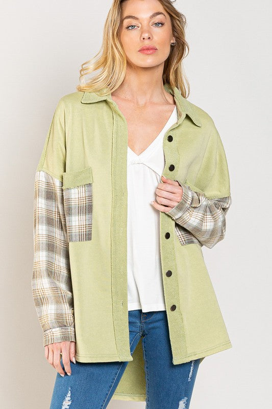 A person wearing the Long Sleeve With Plaid Detail Sleeve Shacket in brown, featuring plaid details on the sleeves and a matching pocket, paired with a white top underneath and a wide-brimmed hat—perfect for transitional weather.