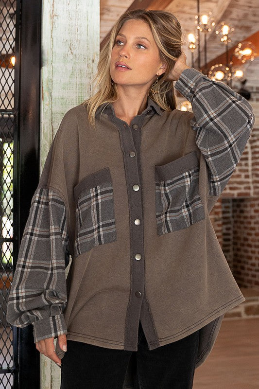 A person wearing the Long Sleeve With Plaid Detail Sleeve Shacket in brown, featuring plaid details on the sleeves and a matching pocket, paired with a white top underneath and a wide-brimmed hat—perfect for transitional weather.