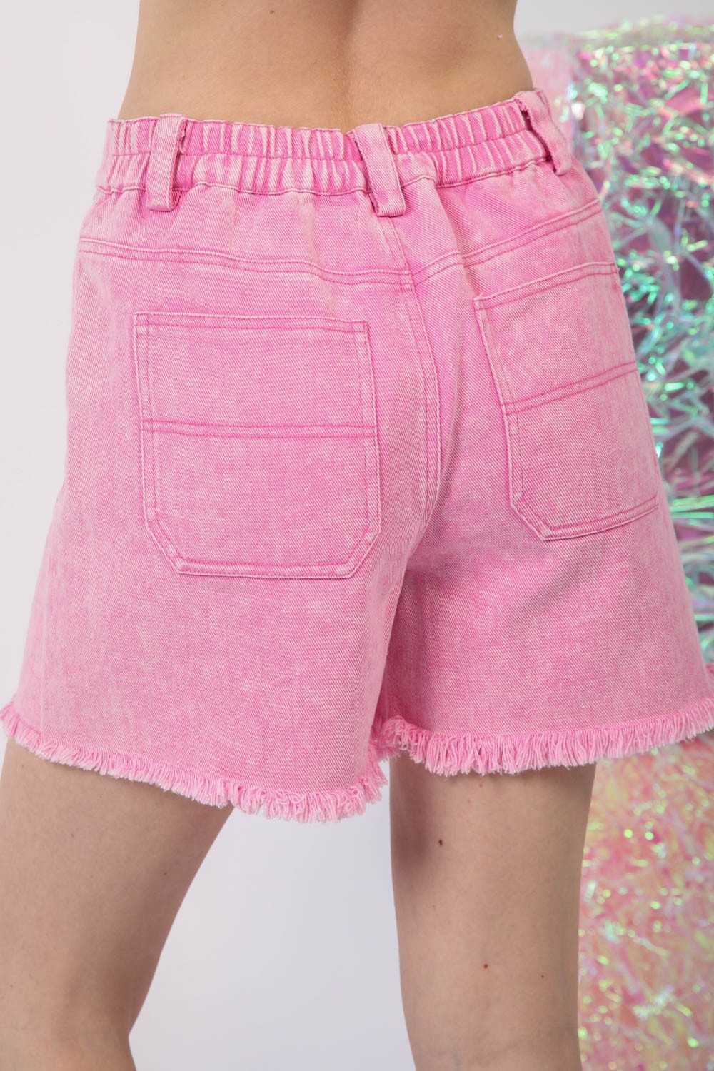 A person embodies the essence of summer fashion in the VERY J Washed Raw Hem Denim Shorts, featuring chic frayed hems and practical front pockets.