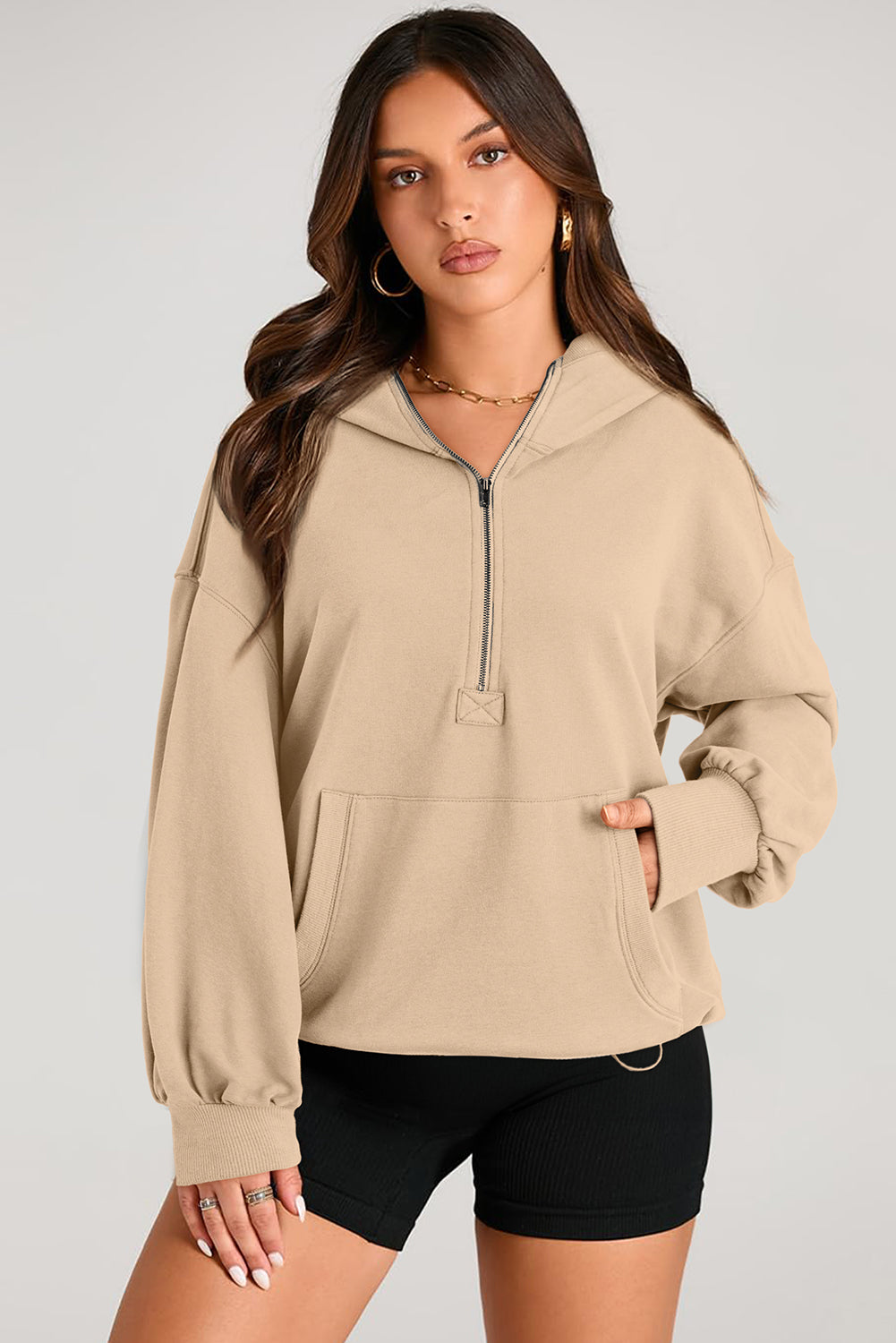 A person with long brown hair is standing with their back to the camera, wearing a Parchment Solid Kangaroo Pocket Half Zipper Oversized Hoodie and black shorts.