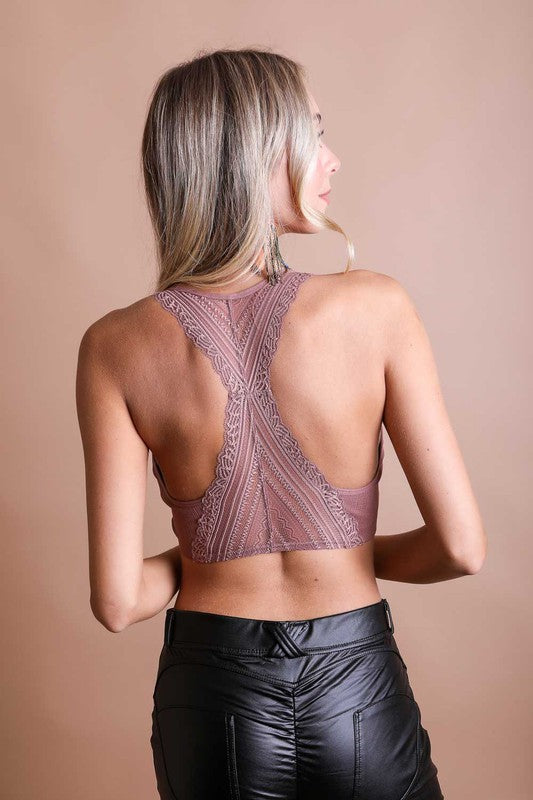 A woman with long blonde hair is shown from behind, wearing a Seamless Front Lace Racerback Bralette with a ribbed fit and high-waisted brown pants against a plain beige background.