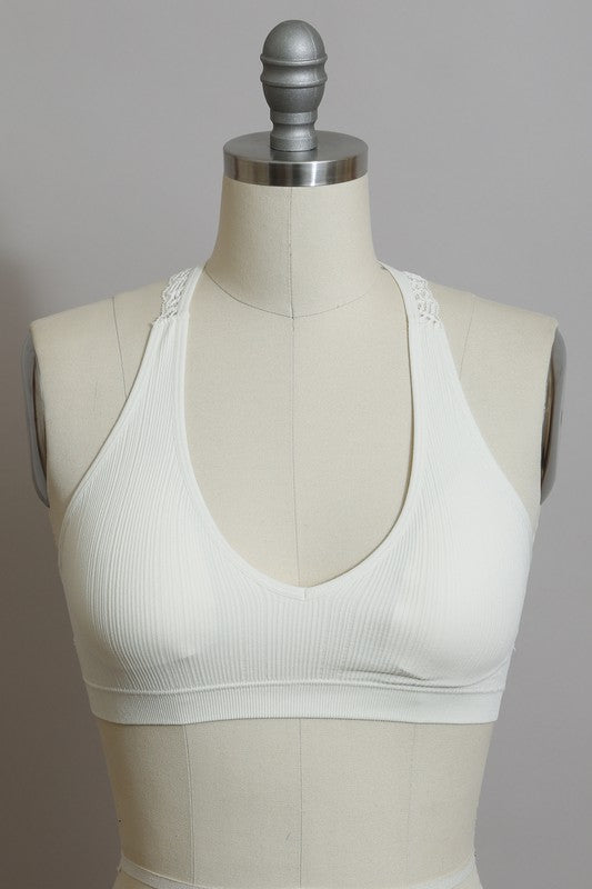 A woman with long blonde hair is shown from behind, wearing a Seamless Front Lace Racerback Bralette with a ribbed fit and high-waisted brown pants against a plain beige background.