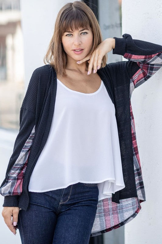 A woman leans against a wooden fence, looking over her shoulder. She is wearing the Plaid Back Waffle Knit Cardigan and jeans, embodying a cozy, effortless style.