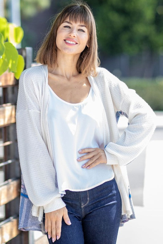 A woman models the Plaid Back Waffle Knit Cardigan paired with black pants, standing against a light background.