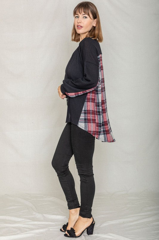 A woman leans against a wooden fence, looking over her shoulder. She is wearing the Plaid Back Waffle Knit Cardigan and jeans, embodying a cozy, effortless style.