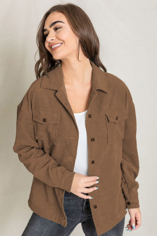 A woman in a light gray Corduroy Boyfriend Oversize Jacket, made in China, stands against a neutral backdrop wearing it over a white top and dark jeans.