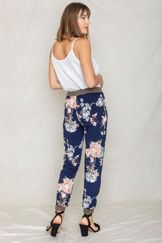 Modeling the Rose Print Jogger, this ensemble highlights a soft polyester and spandex blend with a sleek gray waistband and cuffs, perfectly paired with black heeled sandals to enhance elegance.