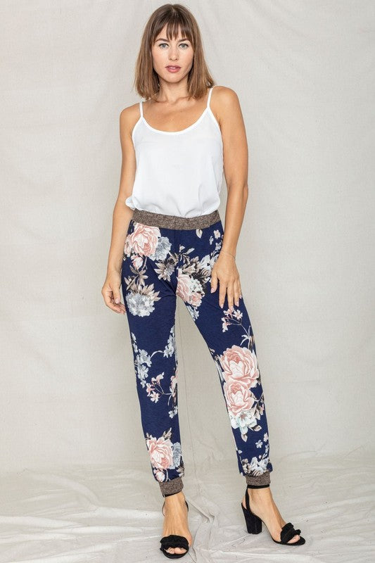 A person wearing Rose Print Joggers, paired with a white top and black heeled sandals, is standing against a light background.