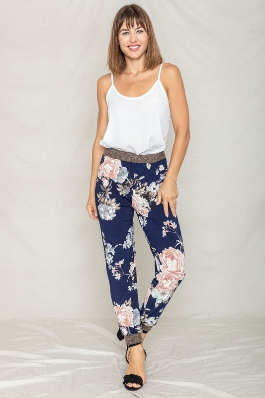 A person wearing a white t-shirt and the Plus Rose Print Jogger stands in front of a neutral backdrop, smiling slightly.