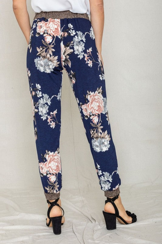 Modeling the Rose Print Jogger, this ensemble highlights a soft polyester and spandex blend with a sleek gray waistband and cuffs, perfectly paired with black heeled sandals to enhance elegance.