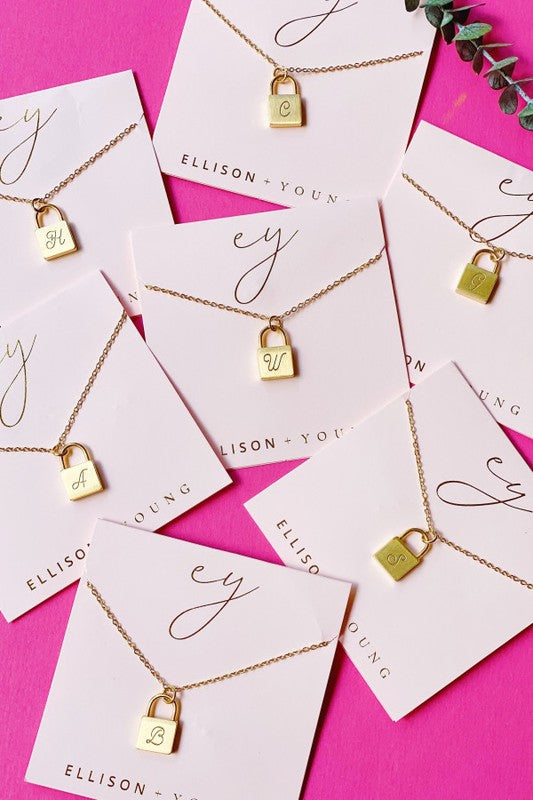 Scripted Notes Locket Initial Necklaces are arranged on white Ellison+Young cards against a pink background.