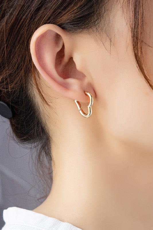 Two Heart Shape Hinged Huggie Hoop Earrings, adorned in gold plating, are displayed on a beige surface.