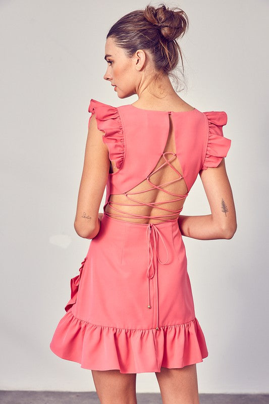 A person wearing the elegant, sleeveless V-Neck Ruffle Dress in chic pink, complete with ruffled shoulders and hem, stands against a plain background—an effortlessly versatile wardrobe staple.