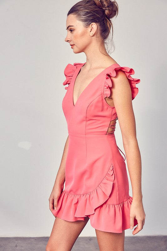 A person wearing the elegant, sleeveless V-Neck Ruffle Dress in chic pink, complete with ruffled shoulders and hem, stands against a plain background—an effortlessly versatile wardrobe staple.