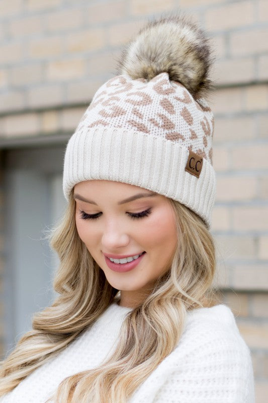 Woman smiling while wearing a pink Leopard Fur Pom Beanie.