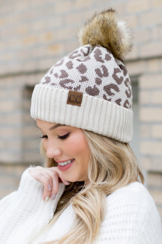 Woman smiling while wearing a pink Leopard Fur Pom Beanie.