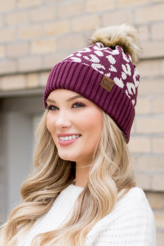 Woman smiling while wearing a pink Leopard Fur Pom Beanie.