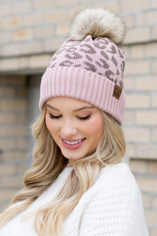 Woman smiling while wearing a pink Leopard Fur Pom Beanie.