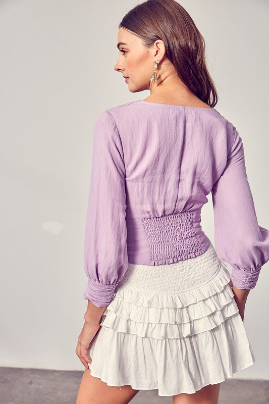 Against a neutral backdrop, a woman showcases elegance and comfort in a stylish Front Tie Long Sleeve Top, perfectly paired with a light blue layered skirt, making it a versatile wardrobe essential.