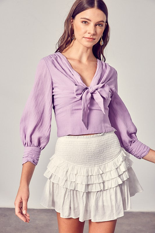 Against a neutral backdrop, a woman showcases elegance and comfort in a stylish Front Tie Long Sleeve Top, perfectly paired with a light blue layered skirt, making it a versatile wardrobe essential.