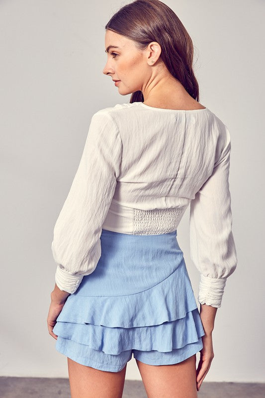 Against a neutral backdrop, a woman showcases elegance and comfort in a stylish Front Tie Long Sleeve Top, perfectly paired with a light blue layered skirt, making it a versatile wardrobe essential.