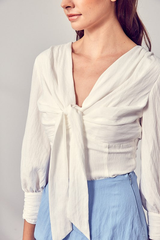 Against a neutral backdrop, a woman showcases elegance and comfort in a stylish Front Tie Long Sleeve Top, perfectly paired with a light blue layered skirt, making it a versatile wardrobe essential.