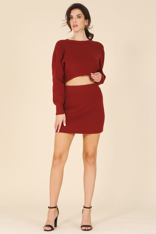 A person is showcasing the Ribbed knit crop top and skirt set in a vibrant red hue, standing out beautifully against a beige background.