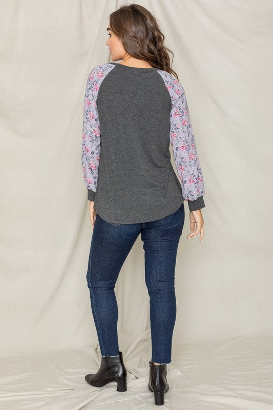 A woman with long hair wears the V-Stich Floral Raglan Sleeve top and stands against a plain backdrop.