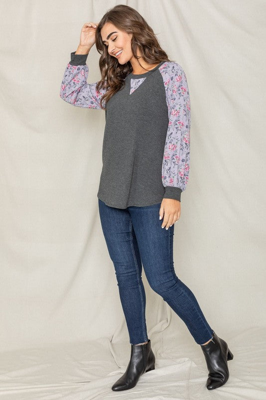 A woman with long hair wears the V-Stich Floral Raglan Sleeve top and stands against a plain backdrop.