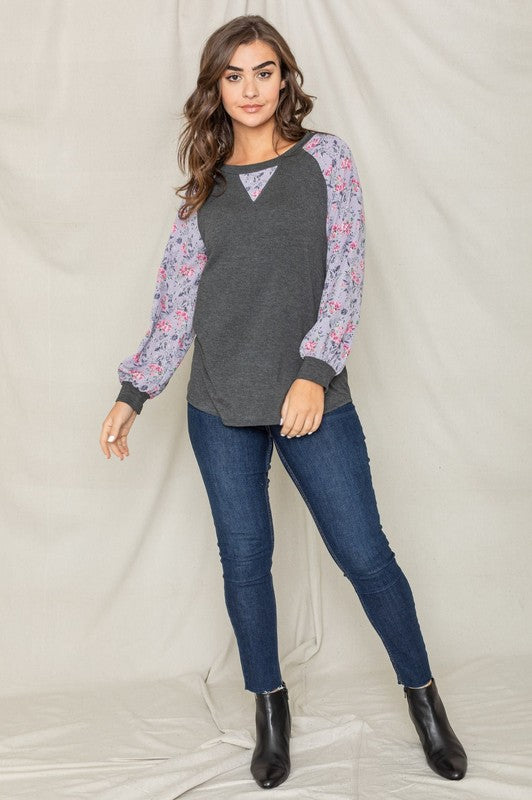 Woman wearing a V-Stitch Floral Raglan Sleeve top, looking at the camera with a neutral expression.