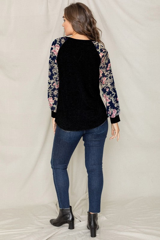 A woman with long hair wears the V-Stich Floral Raglan Sleeve top and stands against a plain backdrop.