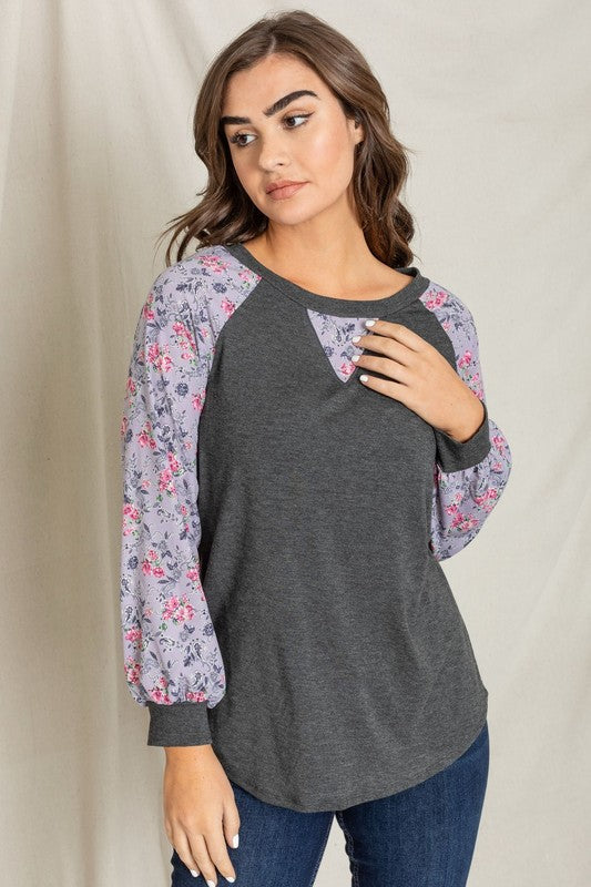 Woman wearing a V-Stitch Floral Raglan Sleeve top, looking at the camera with a neutral expression.