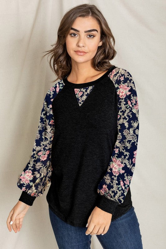 A woman with long hair wears the V-Stich Floral Raglan Sleeve top and stands against a plain backdrop.