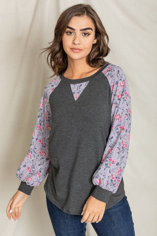 A woman with long hair wears the V-Stich Floral Raglan Sleeve top and stands against a plain backdrop.