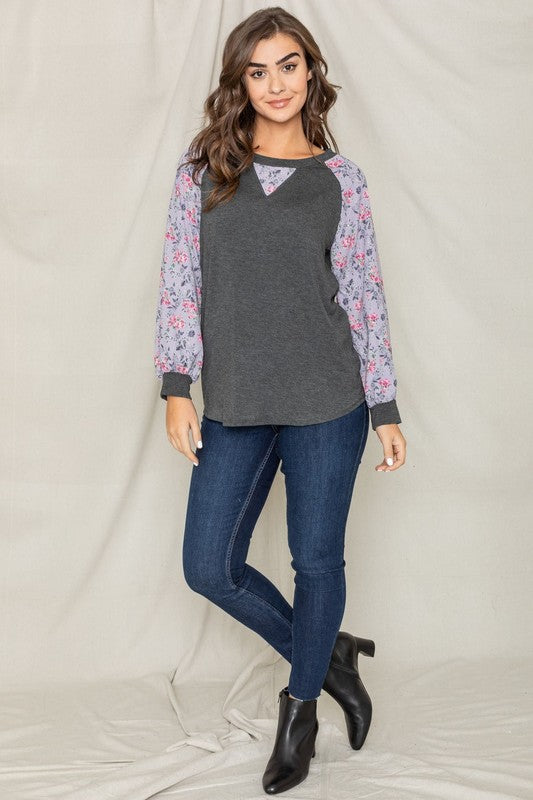 Woman wearing a V-Stitch Floral Raglan Sleeve top, looking at the camera with a neutral expression.