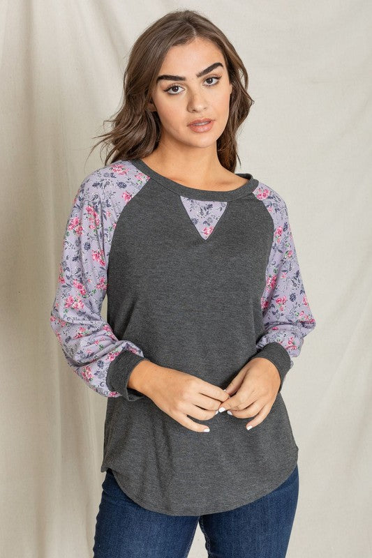 A woman with long hair wears the V-Stich Floral Raglan Sleeve top and stands against a plain backdrop.