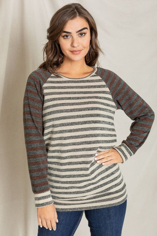 A person with shoulder-length hair is wearing the Two Tone Terry Stripe Tunic, showcasing its distinctive gray and brown stripe pattern. They have matched it with dark pants and are posing against a plain background.