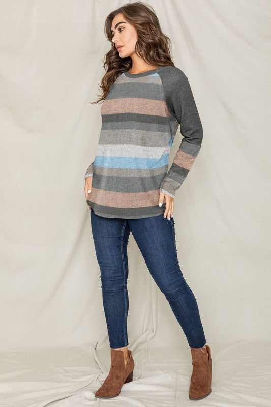 Dressed in the Multi Stripe Tunic paired with jeans, a person stands in a warm, inviting room featuring a plant and couch in the background.