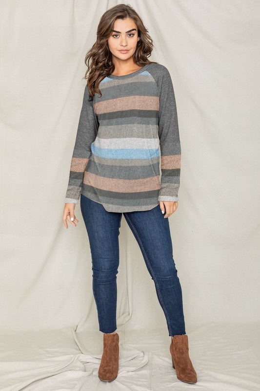 Dressed in the Multi Stripe Tunic paired with jeans, a person stands in a warm, inviting room featuring a plant and couch in the background.