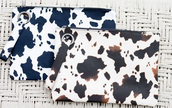 A person flaunts the trending Cow Print Oversized Everyday Clutch, perfectly paired with a cozy oversized gray cardigan, complemented by a black top and ripped jeans.