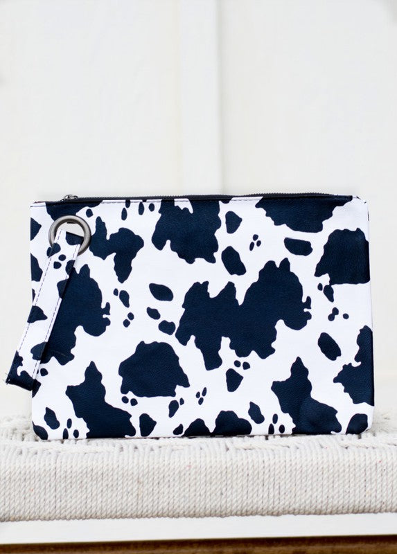 A person flaunts the trending Cow Print Oversized Everyday Clutch, perfectly paired with a cozy oversized gray cardigan, complemented by a black top and ripped jeans.