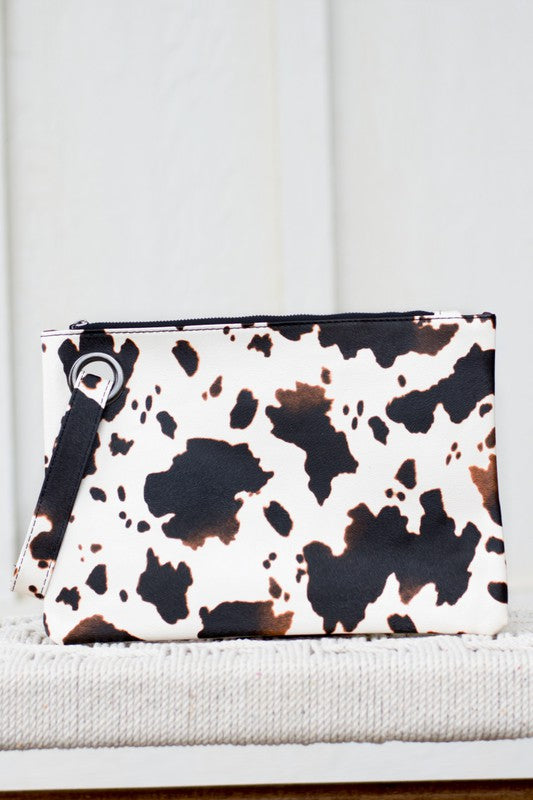 A person flaunts the trending Cow Print Oversized Everyday Clutch, perfectly paired with a cozy oversized gray cardigan, complemented by a black top and ripped jeans.