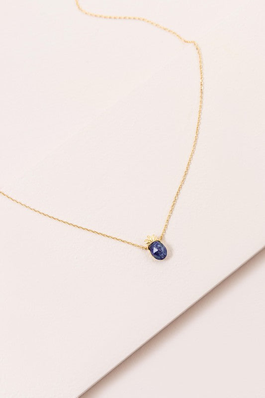 The Pineapple Stone Necklace elegantly showcases a small black oval gemstone pendant on a gold chain, adding a touch of casual jewelry sophistication against the light background.