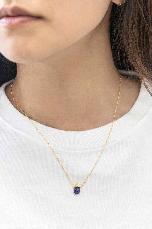 The Pineapple Stone Necklace elegantly showcases a small black oval gemstone pendant on a gold chain, adding a touch of casual jewelry sophistication against the light background.