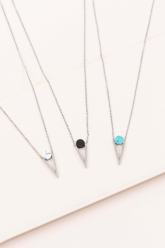 The Tensly Point Stone Necklace Silver collection features three charm necklaces with silver chains, each showcasing a triangular pendant enhanced by a circular accent in black, turquoise, and white. Displayed on a light background, these stainless steel pieces elegantly emphasize the allure of natural stones.