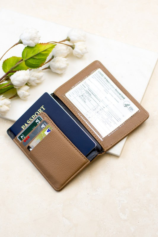 A person wearing a white sweater and blue jeans is holding an open Passport and Vaccine Credit Card Wallet in leopard print, showcasing a passport, vaccine card holder, cards, and a boarding pass.