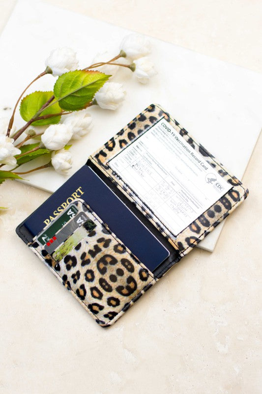 A person holding an open Passport and Vaccine Credit Card Wallet with a leopard print design, displaying a passport, multiple credit cards, boarding pass, and a vaccine card holder.